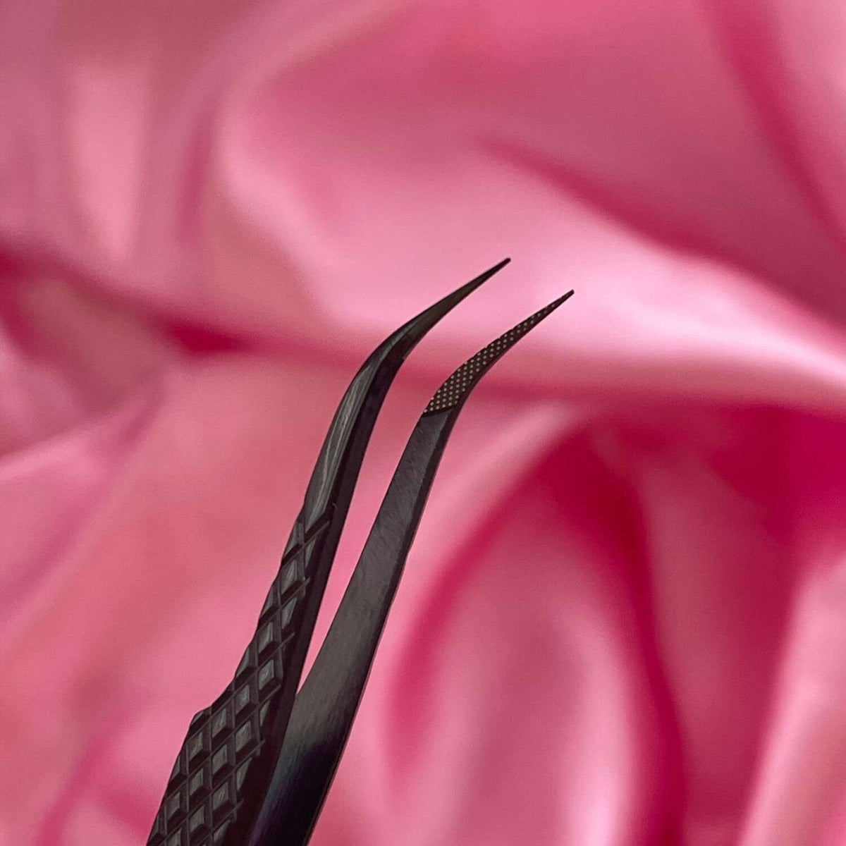 Black precision tweezers with fine tips on a soft pink satin background. Ideal for intricate beauty tasks.