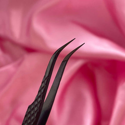 Black precision tweezers with fine tips on a soft pink satin background. Ideal for intricate beauty tasks.