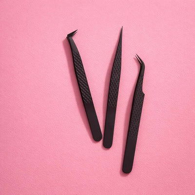 Set of three black precision tweezers with textured grip, ideal for grooming and crafting on pink background.