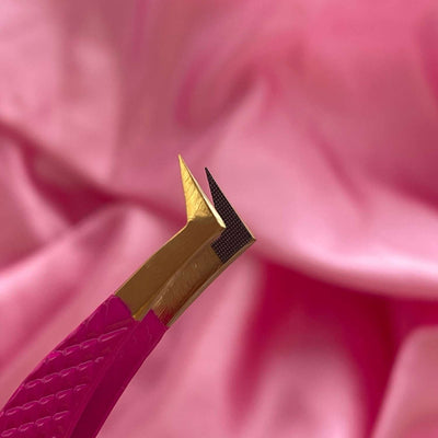 Pink precision tweezers with a stainless steel gold tip for fine detailing on a soft pink fabric background.