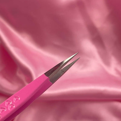 Pink stainless steel tweezers with sharp, precise tips against a soft pink satin background.