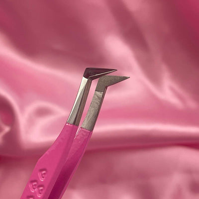 Pink stainless steel tweezers with dual tips on a soft pink satin background. Ideal for precision grooming and styling.
