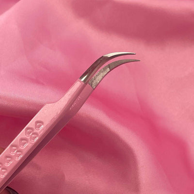 Pink stainless steel tweezers with a curved tip displayed on a soft pink fabric background.