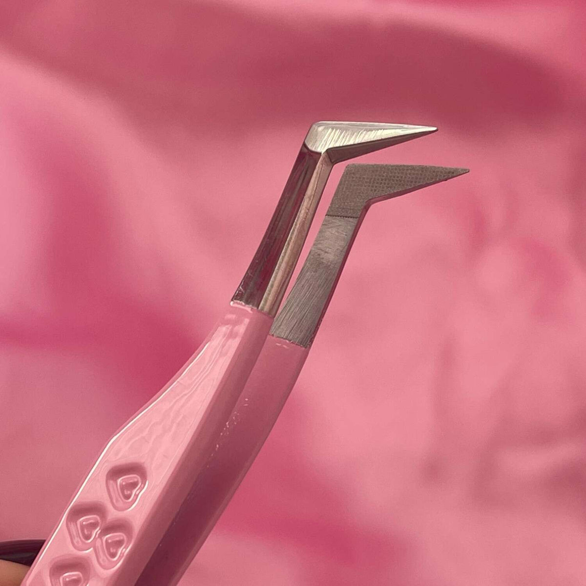 Pink stainless steel tweezers with angled tips for precise application against a soft pink background.