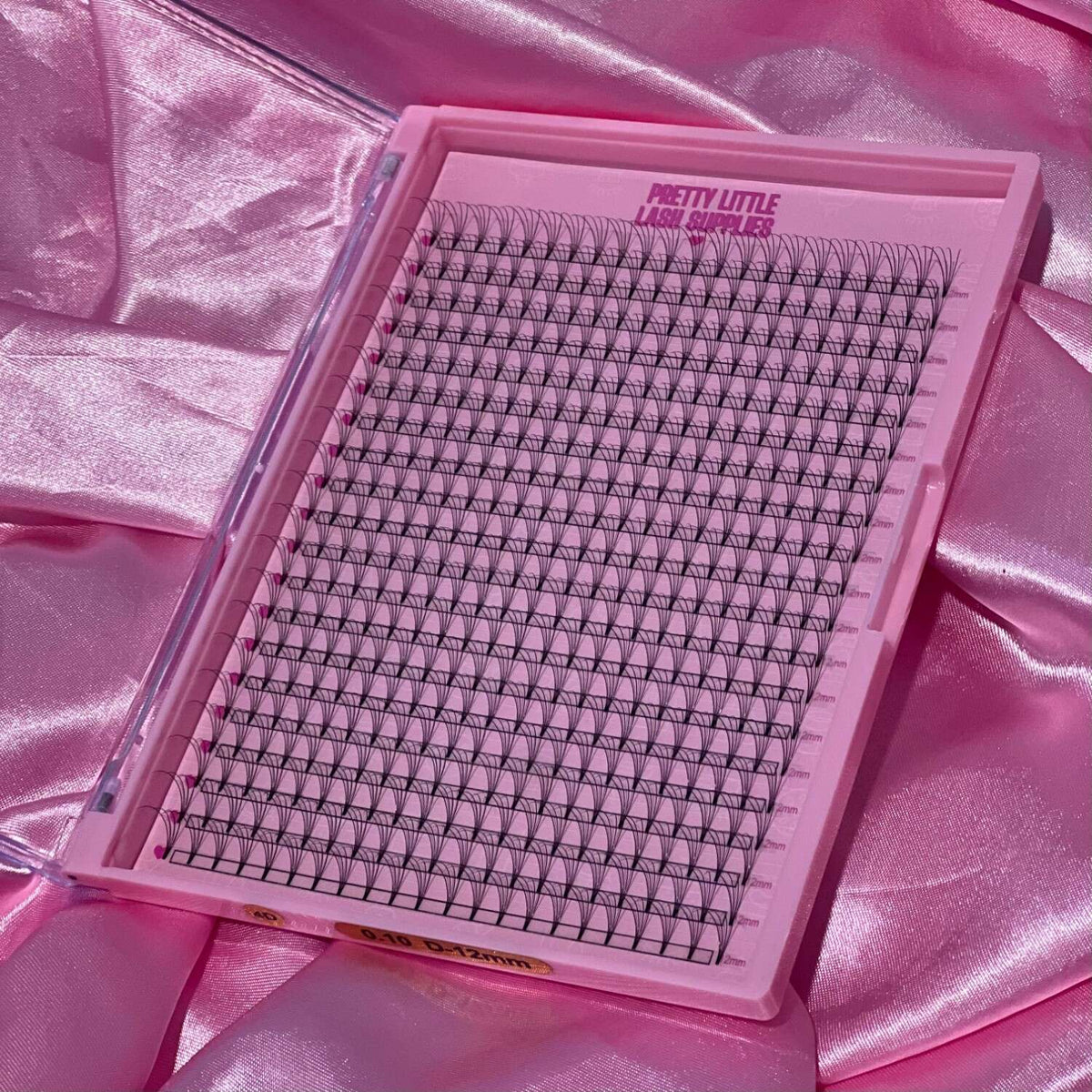 Pink lash extension tray with black lashes arranged in rows, perfect for a sleek and stylish beauty application.